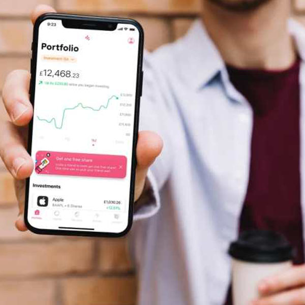 Person holding a smartphone with the FreeTrade app showing a portfolio balance and investment graph, along with Apple shares details.